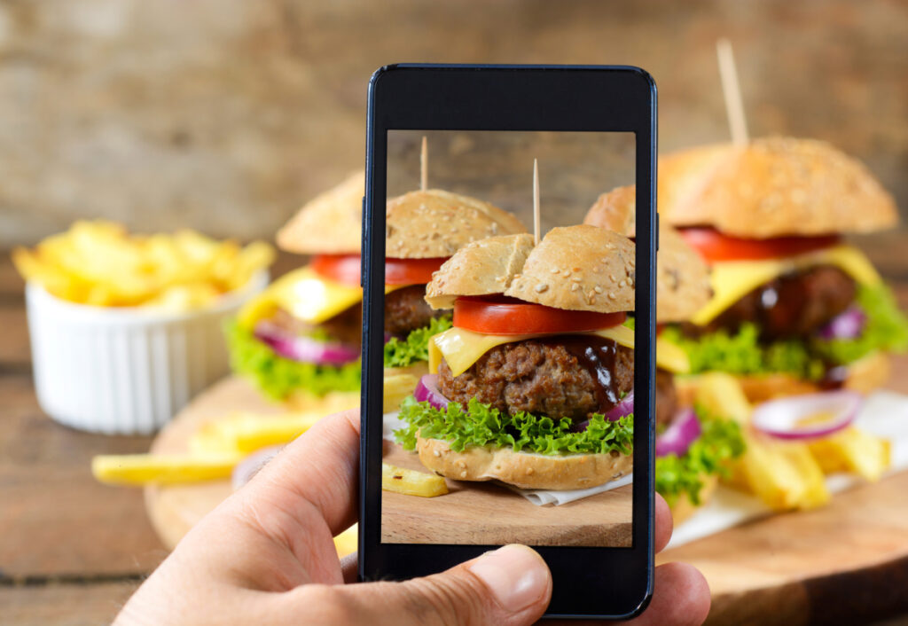 A person takes a snapshot on their smartphone of some delicious cheeseburgers.